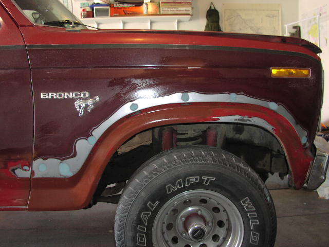 Maroon Ford Bronco fender with body filler around the wheel arch and BRONCO emblem