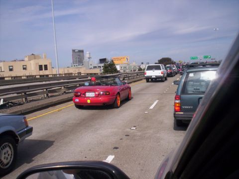 1989 Ford Bronco - A red convertible is driving in traffic on a highway with other vehicles around it.