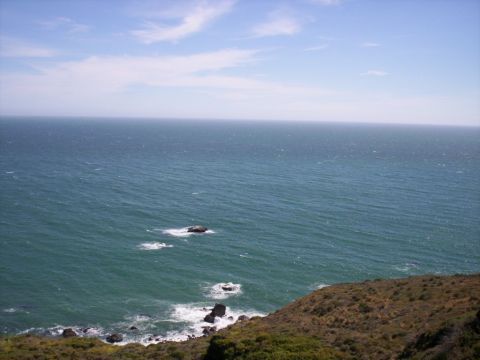 1989 Ford Bronco - A wide view of the ocean and a coastline with sparse vegetation and scattered rocks.