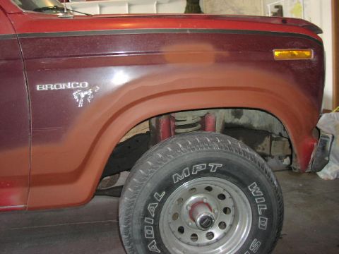 1981 Ford Bronco - The side of a red 1981 Ford Bronco is visible, with the front wheel and fender prominently displayed.