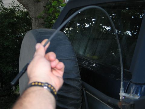 1994 Ford Bronco - A hand holds a car antenna near the rear window of a dark SUV, which has a spare tire cover.