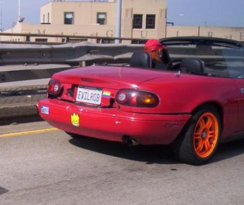 1989 Ford Bronco - Rear view of a red convertible sports car with custom license plate and orange wheels.