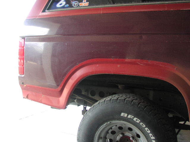 Rear quarter panel and wheel arch of a red Ford SUV with mismatched paint and BFGoodrich tire