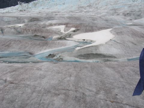 1973 Ford Ranchero - Meltwater streams carve channels across the textured surface of a glacier, with patches of snow and ice visible.