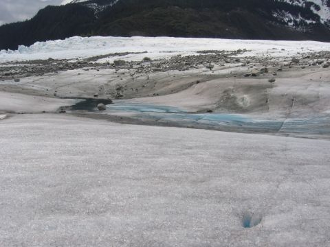 1973 Ford Ranchero - Meltwater pools form on the surface of a glacier, with forested mountains visible in the distance.