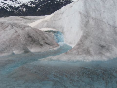 1973 Ford Ranchero - A glacier landscape shows intricate patterns of meltwater carving through the ice, with distant snow-covered mountains under a cloudy sky.