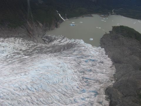 1973 Ford Ranchero - A vast glacier meets a lake dotted with icebergs, with forested mountains in the distance.