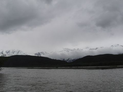 1973 Ford Ranchero - A wide river flows in front of dark hills and snow-covered mountains under a cloudy sky.