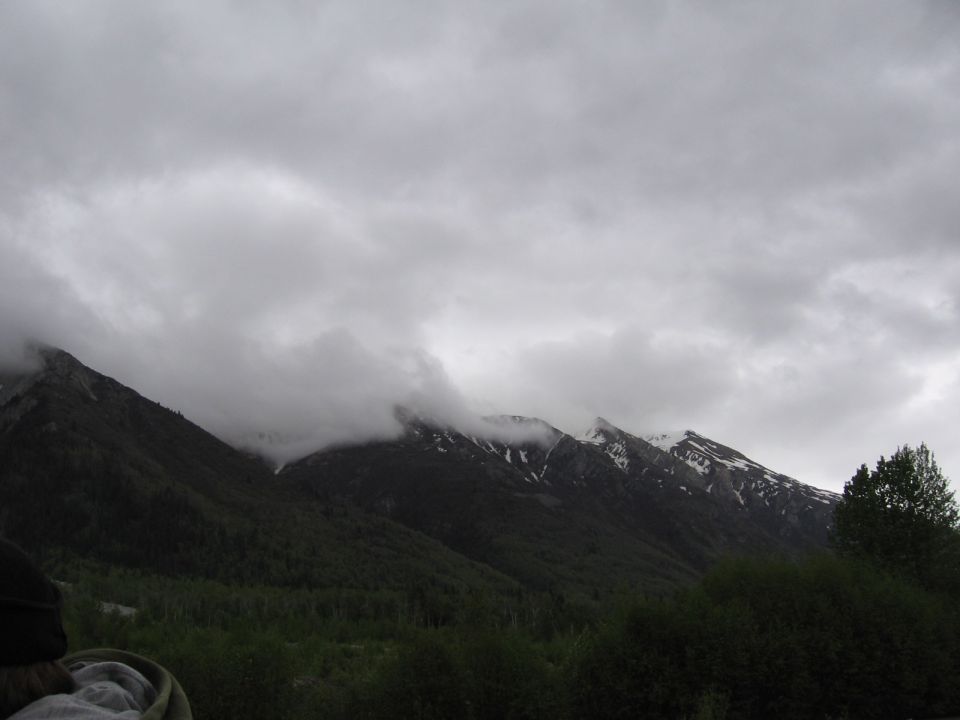 cloudy sky over forested mountains with some snow on peaks