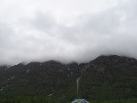 1973 Ford Ranchero - A vast mountain range is shrouded in low-hanging clouds, with a dark forest covering its lower slopes.