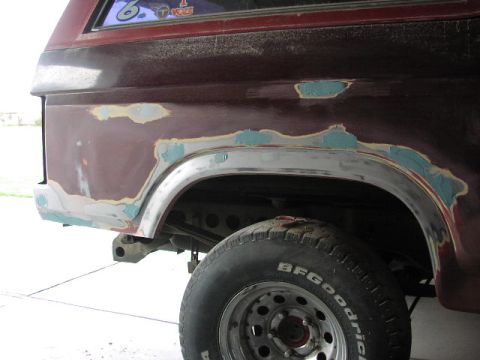 1981 Ford Bronco - Rear fender of a maroon SUV shows areas of body filler and primer, indicating repair work.