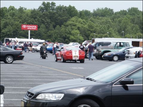 2001 Mercury Grand Marquis - A red Ford Mustang with white racing stripes is parked in a lot with other vehicles and people.