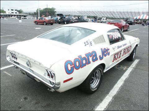 2001 Mercury Grand Marquis - White 1967 Ford Mustang race car with 'Cobra Jet' and 'Rye Ford' graphics is parked at a car show.