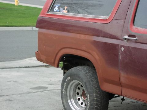 1981 Ford Bronco - Close-up of the rear passenger side of a maroon Ford Bronco, showing the wheel well and part of the door.