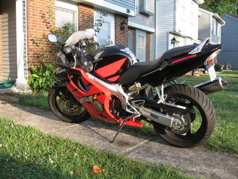 2004 Honda CBR600F - A red and black 2004 Honda CBR600F motorcycle is parked on a sidewalk in front of a house.