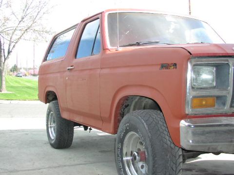 1981 Ford Bronco - Side profile of a red SUV, likely an early 1980s Ford Bronco, parked on pavement.
