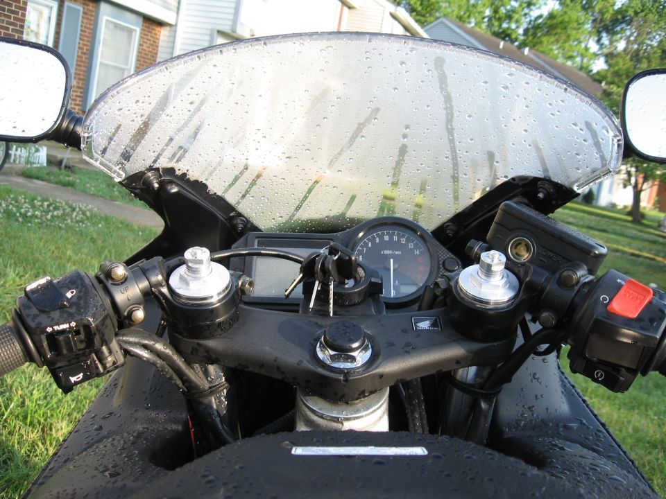 Rain-beaded cockpit of a black Honda sportbike with tachometer and keys in ignition