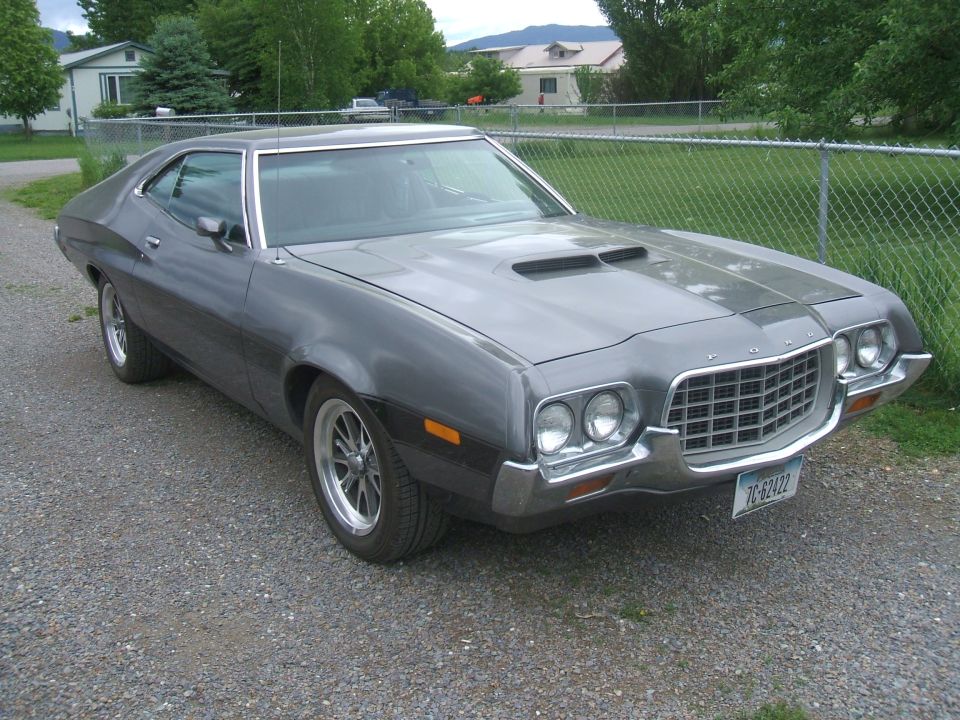 Gray Ford Torino coupe with oval chrome grille and hood scoop parked on gravel