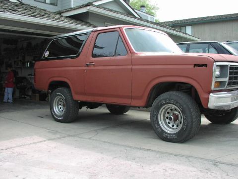 1981 Ford Bronco - A red SUV is parked in front of a garage, with another vehicle visible behind it.