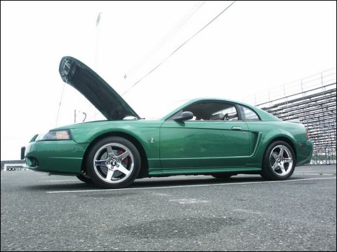 2001 Mercury Grand Marquis - A green Ford Mustang is parked with its hood up, facing a set of bleachers.