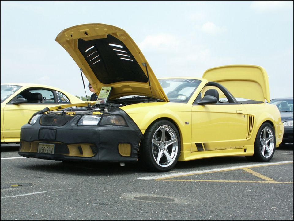 Yellow convertible sports car, hood and trunk open. Another yellow car is visible to the left. License plate reads USC-95N