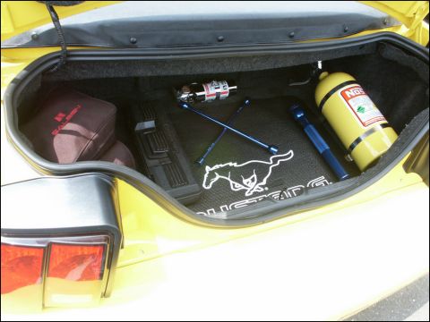 2001 Mercury Grand Marquis - The trunk of a yellow vehicle contains a NOS bottle, a flashlight, and a mat with a Mustang logo.