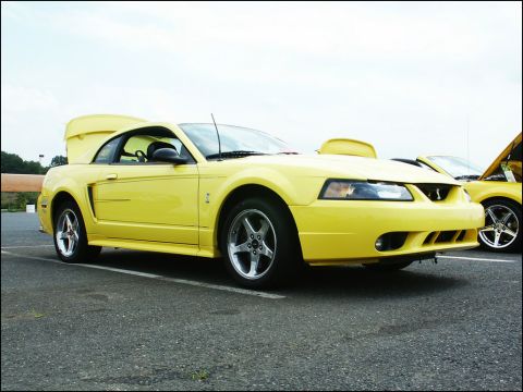 2001 Mercury Grand Marquis - A yellow Ford Mustang is parked at an outdoor event, with another yellow vehicle visible behind it.
