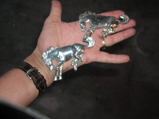 Pair of chrome running-horse vehicle emblems held in an open hand