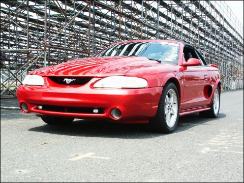 2001 Mercury Grand Marquis - A red Ford Mustang convertible is shown from a three-quarter front view, with a backdrop of stadium seating.