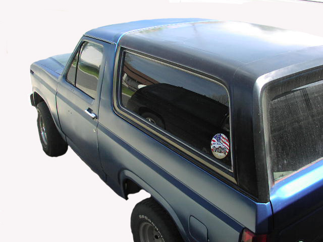 Blue Ford Bronco rear three-quarter view with hardtop and flag decal on glass