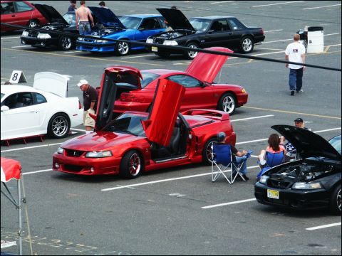 2001 Mercury Grand Marquis - A red convertible with its doors open is displayed at a car show, with other vehicles and spectators around.