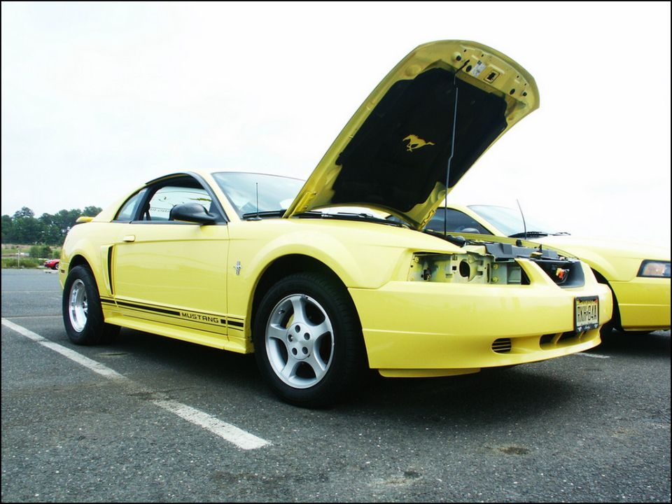 Yellow Ford Mustang with hood open, 'MUSTANG' decal on side. Another yellow car behind it