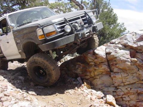 1986 Ford Bronco - Modified Ford Bronco navigates a rocky incline with its front wheels high off the ground.