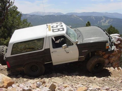 1986 Ford Bronco - This modified Ford Bronco navigates a rocky mountain path, its tires gripping the uneven terrain.