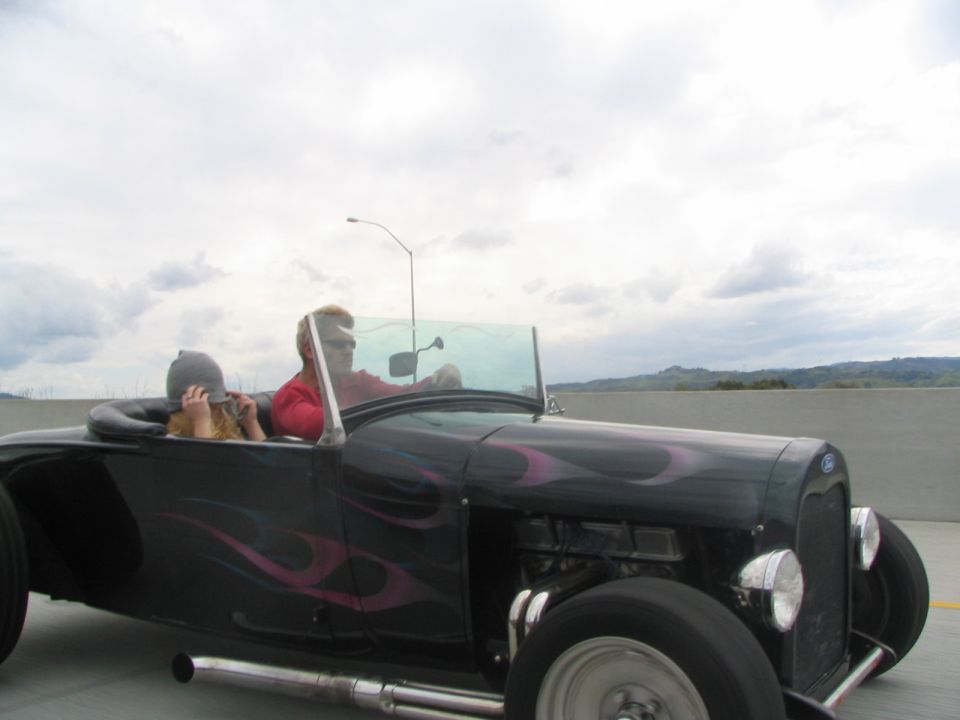 Black hot rod roadster with pink flames, two people inside