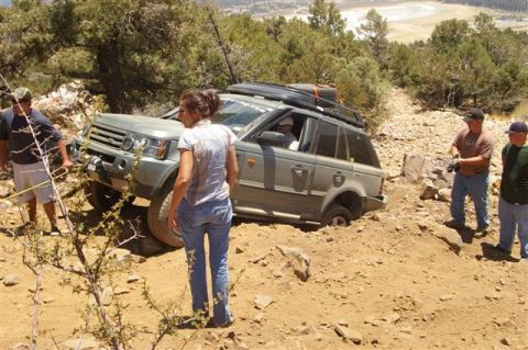 1986 Ford Bronco - People attempt to free an off-road vehicle stuck in a ditch on a dirt path.
