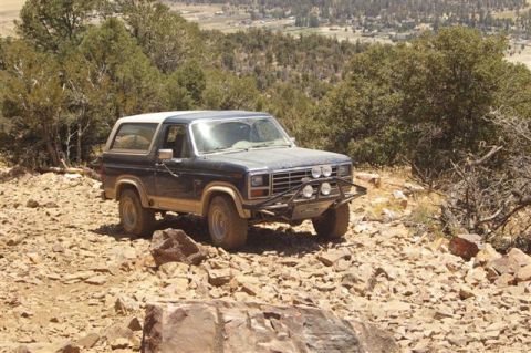 1986 Ford Bronco - A dark blue Ford Bronco navigates a rocky, mountainous terrain under a clear sky.