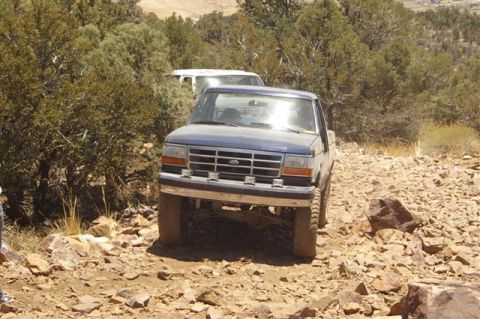 1986 Ford Bronco - A blue Ford F-150 pickup truck navigates a rocky off-road path, with another vehicle visible behind it.