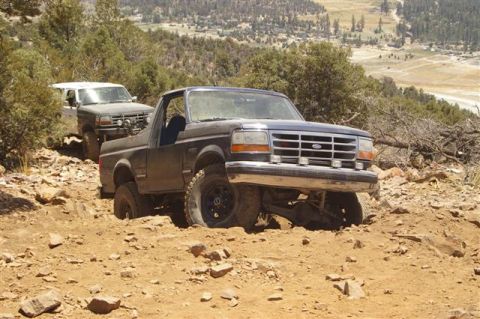 1986 Ford Bronco - Two SUVs tackle a steep, rocky incline on a mountain trail.