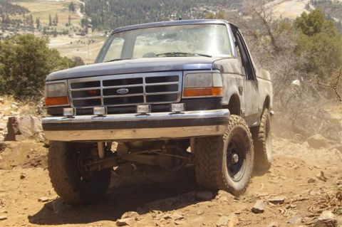 1986 Ford Bronco - A dark blue Ford Bronco navigates a rocky, off-road trail with a mountainous landscape in the background.