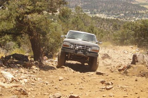 1986 Ford Bronco - Ford Bronco navigates a challenging rocky trail, kicking up dust on its ascent.