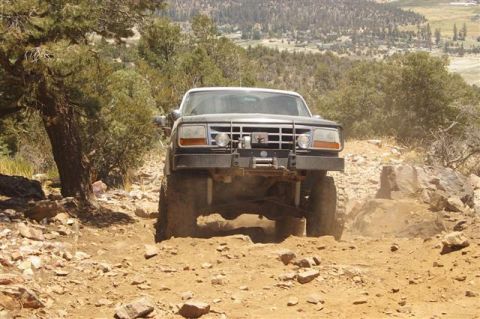 1986 Ford Bronco - A lifted Ford truck navigates a rocky, dusty trail in a mountainous area.