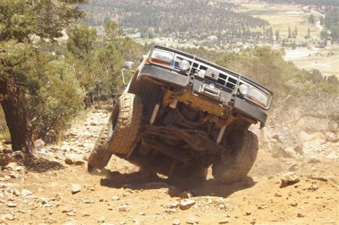1986 Ford Bronco - An off-road vehicle navigates a steep, rocky trail with a valley in the background.