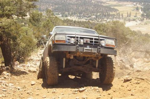 1986 Ford Bronco - This lifted 1987 Ford F-Series truck navigates a challenging, rocky off-road path with a scenic valley in the background.
