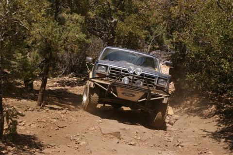 1986 Ford Bronco - A Ford Bronco navigates a steep, rocky off-road path with trees and brush on either side.