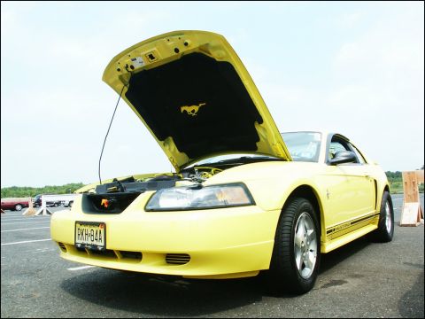 2001 Mercury Grand Marquis - A yellow Ford Mustang is parked with its hood open, revealing the engine and a horse emblem on the underside of the hood.