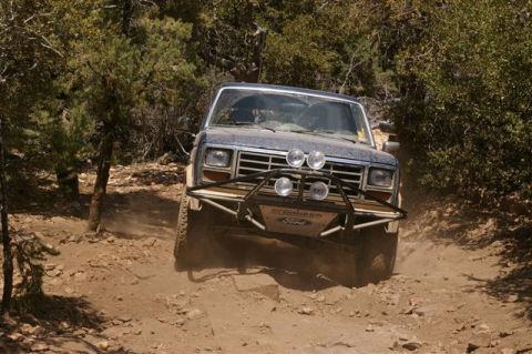 1986 Ford Bronco - A Ford Bronco navigates a rocky, dusty trail surrounded by trees.