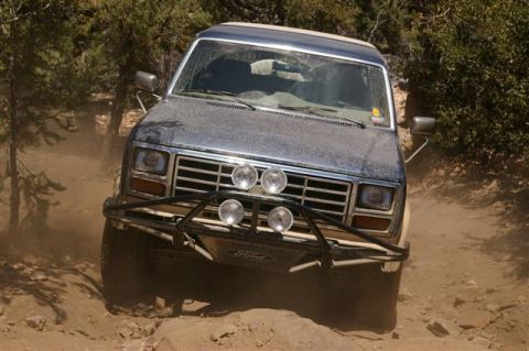 1986 Ford Bronco - 1986 Ford Bronco navigating a rough, off-road path kicking up dust.