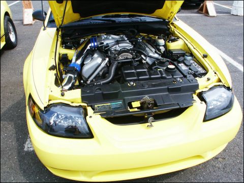 2001 Mercury Grand Marquis - This yellow Ford Mustang has its hood open, revealing the engine compartment. Another vehicle is visible to the left.
