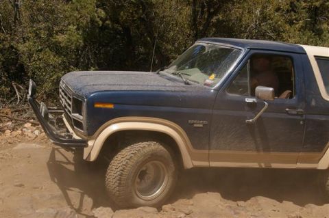 1986 Ford Bronco - A blue Ford Bronco with tan trim is seen from a 3/4 front angle while driving on a rocky, dirt trail.